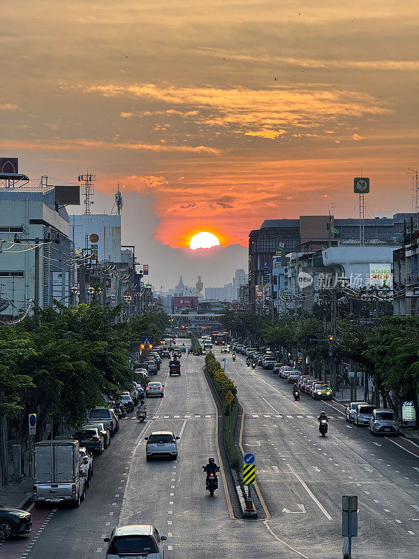 橙色的夕阳天空在佛祖Dhammakaya Thep Mongkol(青铜雕像)和Wat Paknam Bhasicharoen(皇家寺庙)之上，从立交桥上看高速公路上的交通堵塞，摩托车，汽车，空气污染，烟雾，汽车烟雾，重点在前景